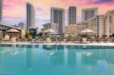 a swimming pool with chairs and umbrellas in a city at Apartment with Balcony - Pool- Near Beach in Hallandale Beach