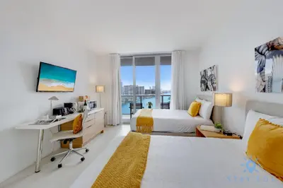 a bedroom with two beds and a desk and a window at Resort Amenities - Amazing Pool and Gym in Hallandale Beach