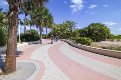 a person riding a bike on a brick path with palm trees at South Beach 2BR with Private Balcony, Walk to Beach in Miami Beach