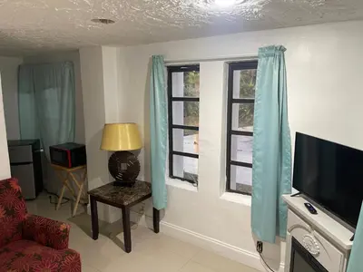 a living room with a tv and two windows at CHEERFUL PRIVATE ROOM 2 MILES AWAY FROM SUNNY ISLES BEACH in North Miami Beach