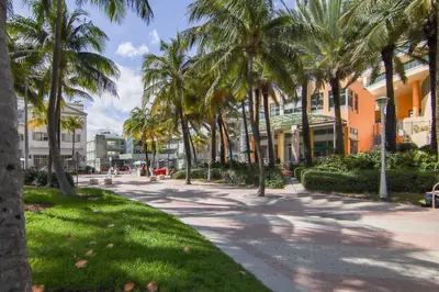 a sidewalk lined with palm trees next to a building at Balcony Deco Apt, w/2 QueenBeds, on Ocean Dr Beach in Miami Beach