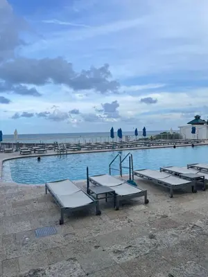 a swimming pool with picnic tables in front of the ocean at Miami Sunny Isles Beach Ocean Front Resort Condo with balcony Pool, Beach,Gym,Valet Parking in Sunny Isles Beach