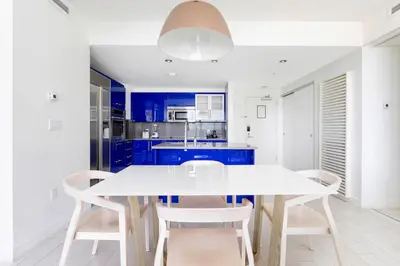 a white kitchen with blue cabinets and a white table and chairs at 2BR W Residence, FLL Beach, Oceanside, pools, hot tub, bar credit in Fort Lauderdale