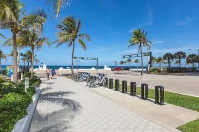 a sidewalk next to a beach with palm trees at 2BR W Residence, FLL Beach, Oceanside, pools, hot tub, bar credit in Fort Lauderdale