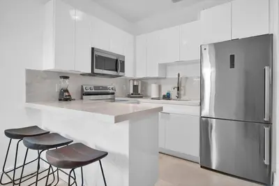 a white kitchen with a refrigerator and two bar stools at Villa 2 in Miami in Miami