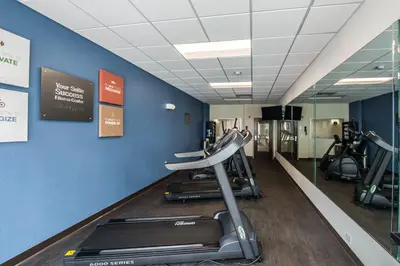 a gym with treadmills and ellipticals on a blue wall at Comfort Suites Fort Lauderdale Airport South & Cruise Port in Dania Beach