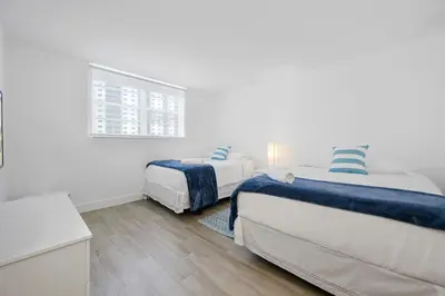 two beds in a room with white walls and wooden floors at Spacious apartment of 2BR - 2BTH in Ocean Reserv front the beach in Sunny Isles Beach
