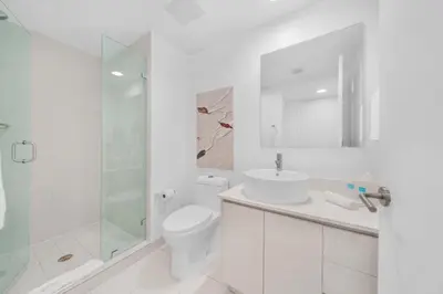 a white bathroom with a toilet and a glass shower at Beachwalk Studio (Beach, Pool and Gym) in Hallandale Beach