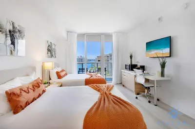 a bedroom with two beds and a desk and a television at Spectacular Infinite View Balcony Pool Gym in Hallandale Beach