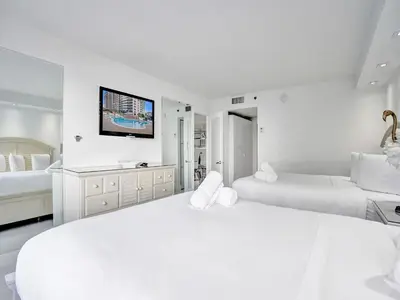 a white bedroom with two beds and a flat screen tv at Beachfront Condo w Beach Service 1207 in Miami Beach