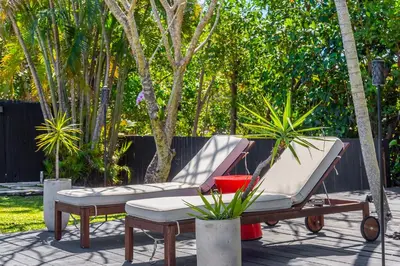 a patio with two chairs and a bench and trees at Casa Olan - Luxury Family Oasis 3BR North Miami Beach Villa with Saltwater Pool & Canal Views in Miami