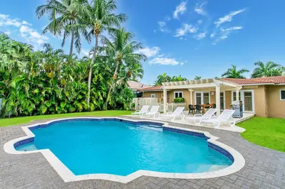 a swimming pool in the backyard of a house with white chairs at Walk to Beach Luxury 5BR & 3BA Villa Hollywood Lakes in Hollywood