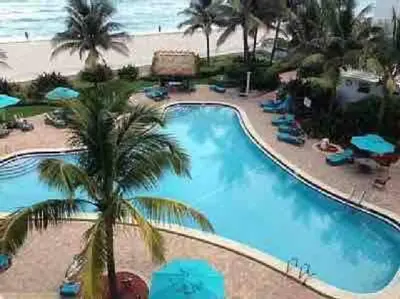 a large swimming pool with palm trees and the ocean at Lovely 2 bedroom with side ocean view in Hollywood