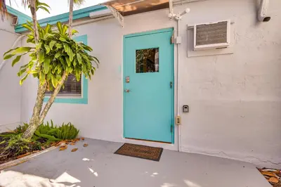a blue door on a white house with a palm tree at Near Haulover Park Hollywood Cottage with Yard! in Hollywood