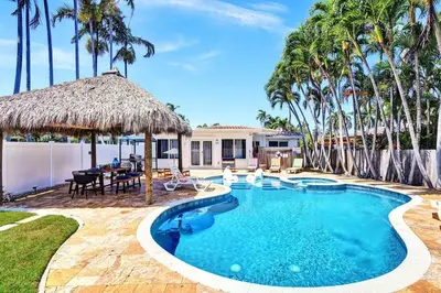 a swimming pool with a straw umbrella and palm trees at Seaside Oasis in Hollywood Lakes near the Beach in Hollywood