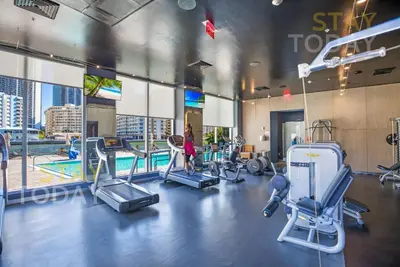 a gym with cardio equipment and a woman in the background at Spacious Luxury Apartment at Beachwalk Resort with Ocean Views and Private Foyer in Hallandale Beach