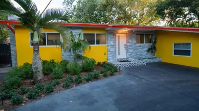 a yellow house with a palm tree and a driveway at Villa Tropical - Your private Miami Resort with a heated pool in North Miami