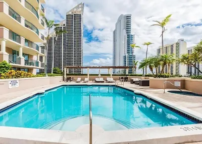 a swimming pool with chairs and palm trees and buildings at Modern 2 BDR at King David with Ocean View in Sunny Isles Beach