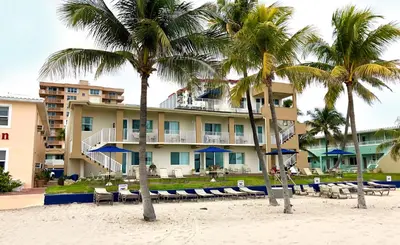 a hotel on the beach with chairs and palm trees at Enchanted Isle Hollywood Beach Resort in Hollywood