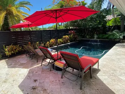 a table and chairs with a red umbrella next to a pool at Riverbank Guesthouse Wilton Manors in Fort Lauderdale