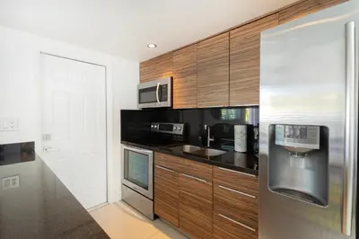 a kitchen with wooden cabinets and a stainless steel refrigerator at GroveO4 10 min from the Beach in Miami