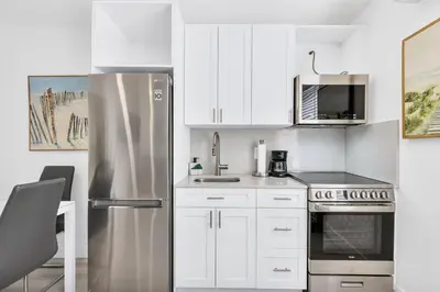 a kitchen with white cabinets and a stainless steel refrigerator at ULTRA Modern Apartment by the Beach in Hollywood