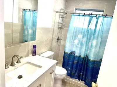 a bathroom with a toilet and a blue shower curtain at Bright & Cozy Family Home Near Dania Beach in Dania Beach