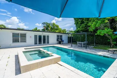 a swimming pool with an umbrella next to a house at Spacious 5 Bedroom Heated Pool and Hot Tub, 12 minutes to the Beach in Hollywood