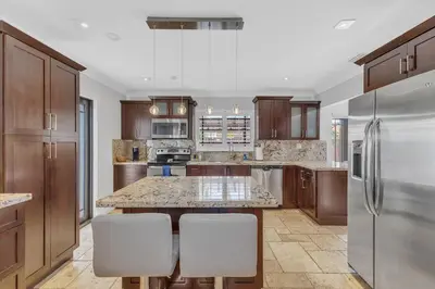 a kitchen with wooden cabinets and a kitchen island with white chairs at Tropical Oasis with Heated Pool and BBQ in Tamiami