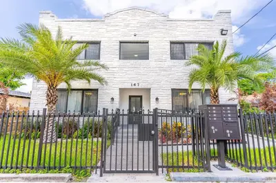 a white house with palm trees in front of a fence at Magical bright Apt 5min walking Design District apt 5 in Miami