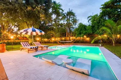 a swimming pool with two chairs and an umbrella at Stunning Historic Villa with Jacuzzi Heated Pool and Resort style Backyard in Miami