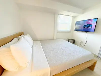 a bedroom with a white bed with a tv on the wall at Modern Miami Family Cottage Beach 15 min in Miami