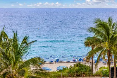 a beach with blue and white umbrellas and palm trees at Oceanfront Luxury Condo with Stunning Views and Resort Amenities in Hollywood