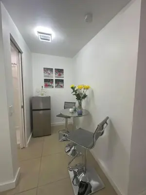 a white room with a table and a counter with flowers at Relaxing Studio Getaway w BBQ, Patio and Parking in Pembroke Pines