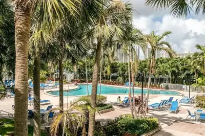 a pool with palm trees and blue chairs at Modern 1 BR Condo, Steps from Beach, Free Parking! in Sunny Isles Beach