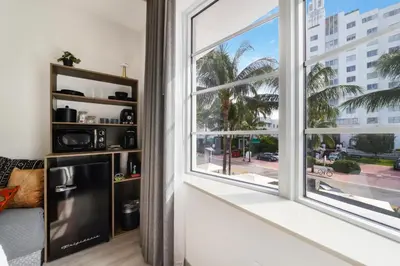 a room with a large window and a black refrigerator at Claremont Hotel in Miami Beach