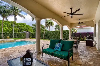a patio with a green couch and a table and a pool at Luxury Tropical Living , 4BR w Backyard Pool Oasis in Hialeah