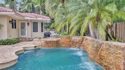 a swimming pool with a waterfall and a stone wall at 5mins to Beach • Pool Hot Tub • Billiards Coral Ridge Getaway by AvantStay in Fort Lauderdale