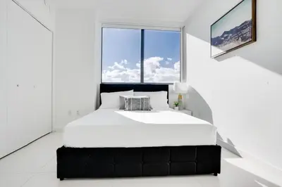 a large bed in a white room with a large window at Miami Paraiso- Rooftop pool views and prime location in Miami