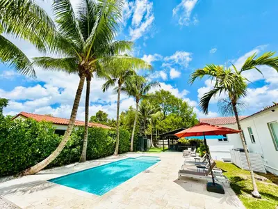 a villa with a swimming pool and palm trees at Heated Pool Tropical House with Summer Kitchen 3BR- Oasis in Miami! in Miami