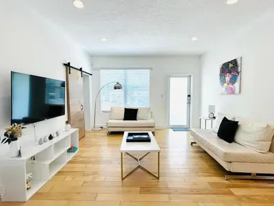 a living room with white furniture and a large screen tv at Heated Pool Tropical House with Summer Kitchen 3BR- Oasis in Miami! in Miami