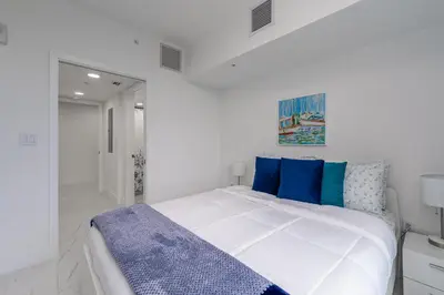 a white bedroom with a bed with blue pillows at Stylish Apt with Pool and Gym near beach in Hollywood