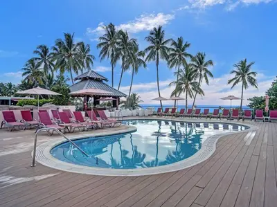 a swimming pool with chairs and palm trees and the ocean at Cozy Ocean View Condo Beach Service 610 in Miami Beach