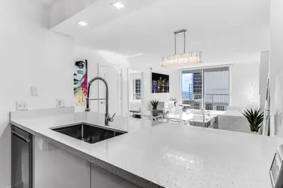 a white kitchen with a sink and a living room at Magnificent Ocean Sky Residence in Miami