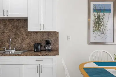 a kitchen with white cabinets and a sink and a table at Sunset Inn - Hallandale Beach in Hallandale Beach