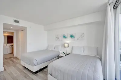 a white bedroom with two beds and a window at Beachwalk Resort in Hallandale Beach