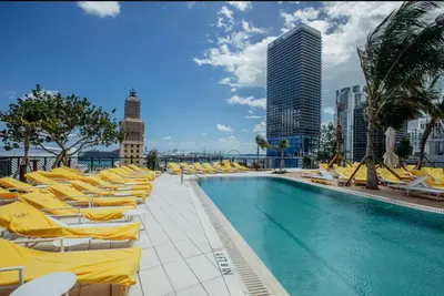 a swimming pool with yellow lounge chairs and a building at Lux 48th Floor Condo, Water views, Pool, Gym and Spa in Miami