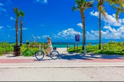 a woman riding a bike on a sidewalk near the beach at Castle 929 Stunning ocean view, pool, beach access, tennis, free parking in Miami Beach