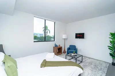 a white bedroom with a bed and a blue chair at Central Miami 1BR Suite Close to Beach & Downtown in Miami