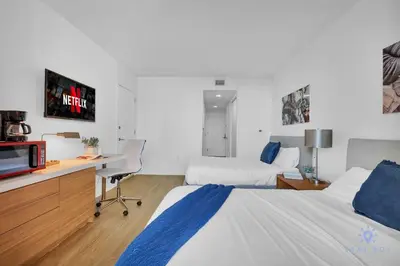 a hotel room with two beds and a desk with a tv at Spectacular Near Beach - 2 BR Apartment in Hallandale Beach